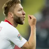 Piłkarz w białej koszulce z numerem 7, Jakub Błaszczykowski, pokazuje gest. Jego błyszczący wzrost na boisku to inspiracja dla wielu.