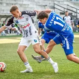 Piłkarze walczą o piłkę na boisku. Jeden w białej koszulce, drugi w niebieskiej z numerem 11. Emocje jak w walce o 3. liga tabelę.