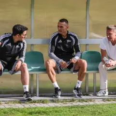Trzech mężczyzn siedzi na ławce. Dwóch w strojach sportowych, jeden w białej koszulce. To trener Lechii Gdańsk i jego współpracownicy.