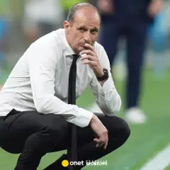 Zamyślony trener Napoli w białej koszuli i czarnym krawacie kuca na boisku, analizując grę.