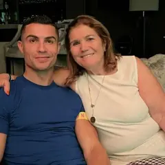 Cristiano Ronaldo z mamą, **Maria Dolores dos Santos Aveiro**, uśmiechają się do zdjęcia, siedząc na kanapie.