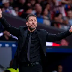 Diego Simeone, trener Atletico, w czarnym garniturze z rozłożonymi rękami, gestykuluje na boisku.