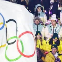 Młodzi sportowcy w barwach narodowych, z flagą olimpijską w tle, czekają na start reprezentacji Polski na Zimowe Igrzyska Olimpijskie 2026.