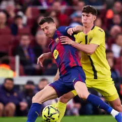 Piłkarz Barcelony Robert Lewandowski w akcji, walczy o piłkę z obrońcą. Kibice na trybunach obserwują mecz, martwiąc się o lewandowski kontuzja.