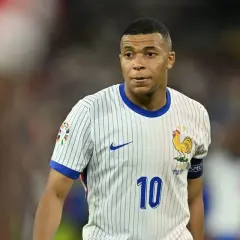 Kylian Mbappé w białej koszulce z numerem 10 i symbolem koguta, reprezentujący Francję. Jego obecne drużyny to PSG i reprezentacja Francji.