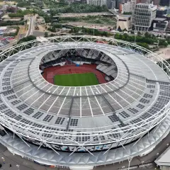 Widok z lotu ptaka na londyński stadion z zieloną murawą i bieżnią. Dach pokryty panelami słonecznymi.
