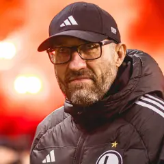 Łukasz Morawski w czapce i okularach, na tle czerwonych rac.