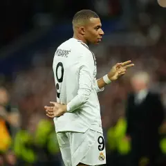 Mbappe, w białej koszulce z numerem 9, gestykuluje na boisku. Jego wzrost robi wrażenie, a kibice śledzą każdy jego ruch.