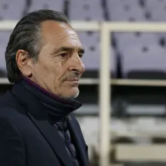 Prandelli, zamyślony trener, w ciemnej kurtce i marynarce, z fioletowym kołnierzem, na tle pustych trybun.