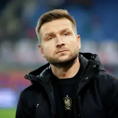 Mężczyzna w czarnej kurtce, z zarostem, w tle trybuny. To piast gliwice trener.