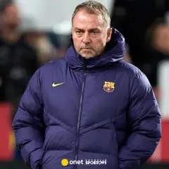 Zamyślony trener Barcelony w granatowej kurtce z herbem klubu.