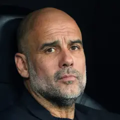 Pep Guardiola, zamyślony trener, siedzi na ławce, analizując grę.