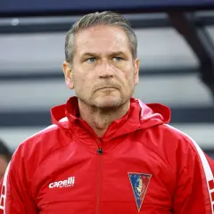 Twarz trenera Pogoni Szczecin, zamyślony, w czerwonej kurtce sportowej z herbem klubu.