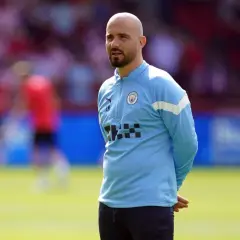 Łysy mężczyzna z brodą, trener Manchester City, w błękitnej bluzie treningowej, stoi na boisku.