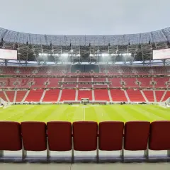 Pusta, nowoczesna arena sportowa w Budapeszcie, z rzędami czerwonych siedzeń i zieloną murawą.