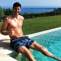 Robert Lewandowski w szortach z motywem liści siedzi na brzegu basenu, dając kciuk w górę. W tle błękitne morze i zieleń.