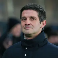 Mężczyzna w ciemnej kurtce, z siwiejącymi włosami, wygląda jak inter trener podczas meczu.