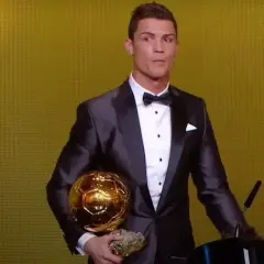 Cristiano Ronaldo w garniturze trzyma złotą piłkę. Ile złotych piłek ma Ronaldo? To pytanie zadaje sobie wielu fanów.