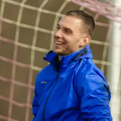 Uśmiechnięty piłkarz w niebieskiej kurtce, gotowy do gry w stylu tiki-taka.