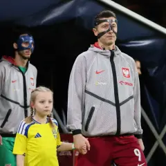 Polscy piłkarze, w tym Robert Lewandowski, wychodzą na murawę z dziećmi. Jeden z zawodników ma niebieską maskę.