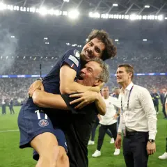 Radość piłkarza PSG obejmującego trenera. W tle tłum kibiców i stadion.