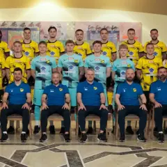 Cała drużyna Wieczysta Kraków w komplecie, pozująca do zdjęcia. Piłkarze w żółtych strojach i sztab szkoleniowy w niebieskich.