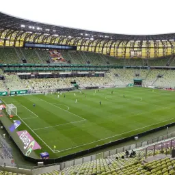 Stadion Lechii Gdańsk, z zielonymi trybunami i murawą, gotowy na mecz. Jego pojemność robi wrażenie.