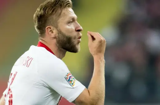 Piłkarz w białej koszulce z numerem 7, Jakub Błaszczykowski, pokazuje gest. Jego błyszczący wzrost na boisku to inspiracja dla wielu.
