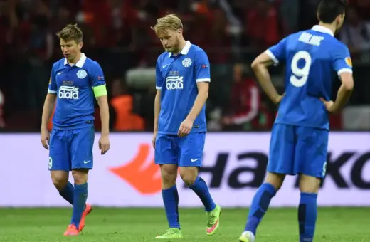 Smutni piłkarze Dnipro Dniepropietrowsk w niebieskich strojach schodzą z boiska po przegranym meczu.