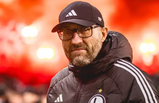 Łukasz Morawski w czapce i okularach, na tle czerwonych rac.