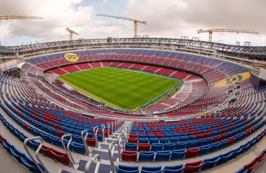 Widok na pusty stadion z czerwono-niebieskimi trybunami, zieloną murawą i dźwigami w tle. To z pewnością najładniejszy stadion w Polsce, czekający na kibiców.
