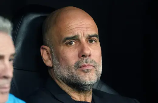 Pep Guardiola, zamyślony trener, siedzi na ławce, analizując grę.