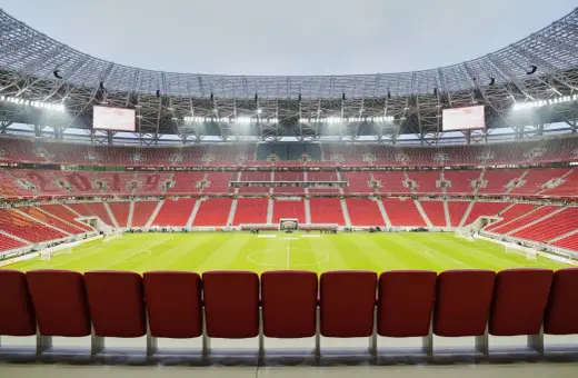 Pusta, nowoczesna arena sportowa w Budapeszcie, z rzędami czerwonych siedzeń i zieloną murawą.