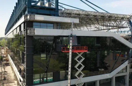Prace przy stadionie Wisły po remoncie. Dwóch robotników na podnośniku montuje szklaną fasadę.
