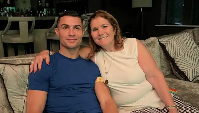 Cristiano Ronaldo z mamą, **Maria Dolores dos Santos Aveiro**, uśmiechają się do zdjęcia, siedząc na kanapie.