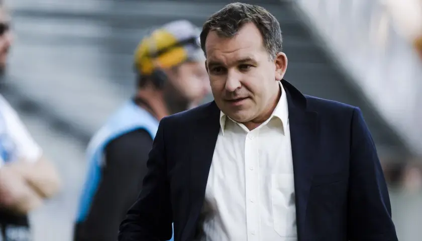 Żyżyński dziennikarz sportowy w garniturze, z uwagą obserwuje wydarzenia na boisku.
