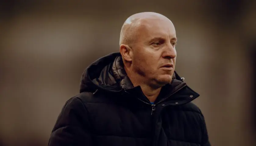 Nowy trener Widzewa, łysy mężczyzna w czarnej kurtce, patrzy w bok z zamyśloną miną.