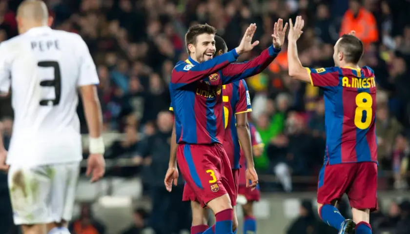 Piłkarze Barcelony, Piqué i Iniesta, świętują bramkę. Na pierwszym planie zawodnik w białej koszulce z numerem 3.