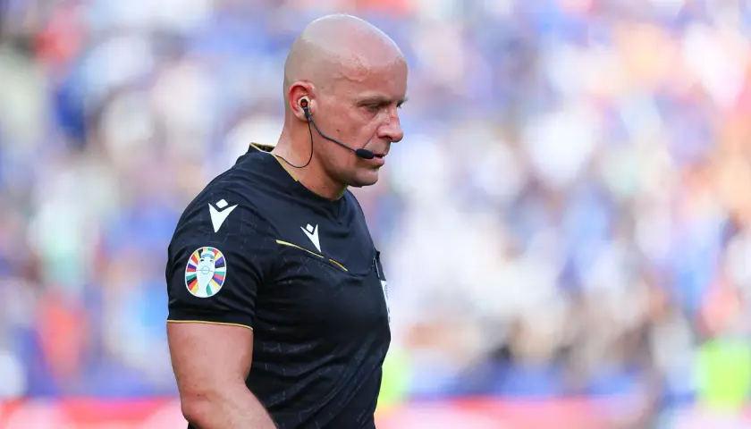 Sędzia Michael Oliver w czarnej koszulce z naszywką Ligi Mistrzów, skupiony na boisku.