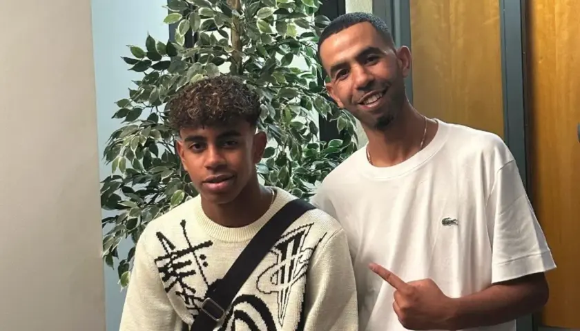 Mounir Nasraoui z młodym chłopcem pozują do zdjęcia obok sztucznej rośliny.