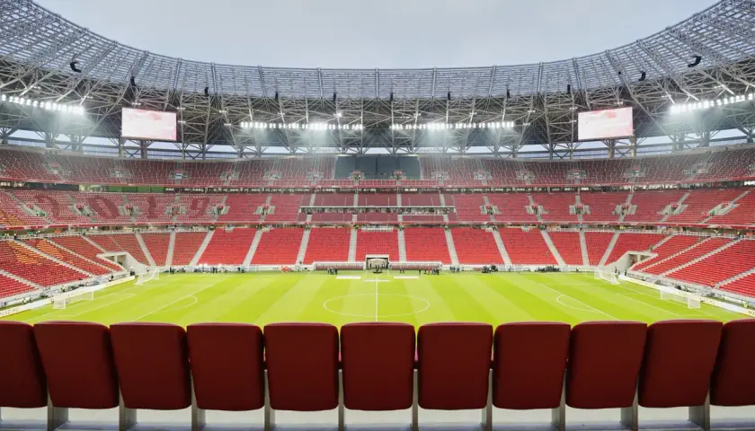 Pusta, nowoczesna arena sportowa w Budapeszcie, z rzędami czerwonych siedzeń i zieloną murawą.