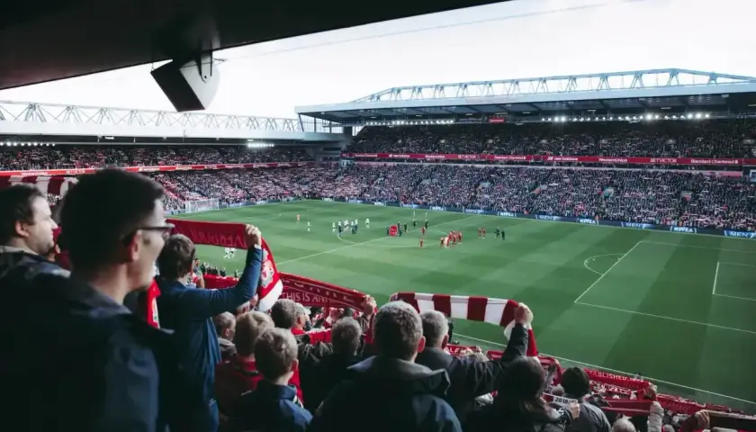 Kibice na stadionie, z szalikami w dłoniach, czekają na wznowienie gry. Zastanawiają się, ile trwa przerwa w meczu.