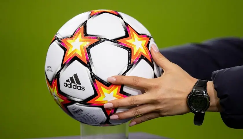 Dłoń z zegarkiem trzyma piłkę Adidas z gwiazdami, gotową do gry w ulubionym klubie piłkarskim na boisku.