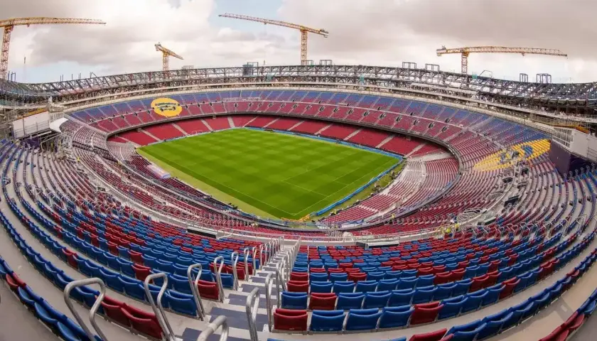 Widok na nowy stadion Barcelony w trakcie budowy. Żurawie górują nad trybunami w barwach klubu, a murawa lśni zielenią.