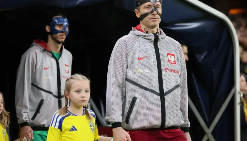 Polscy piłkarze, w tym Robert Lewandowski, wychodzą na murawę z dziećmi. Jeden z zawodników ma niebieską maskę.