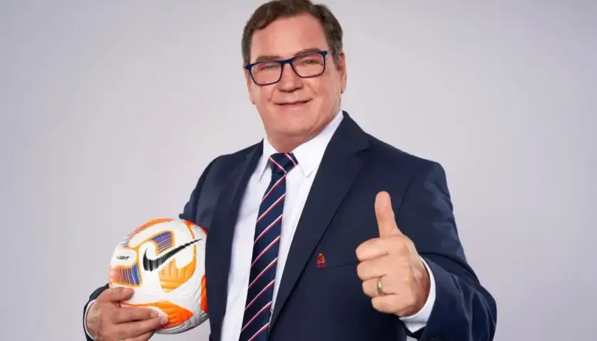 Uśmiechnięty trener reprezentacji Polski w garniturze trzyma piłkę i pokazuje kciuk w górę.