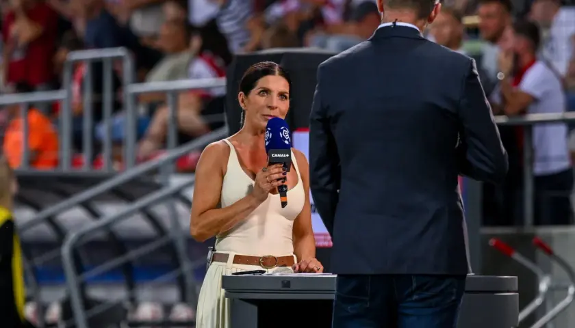 Kobieta z mikrofonem Canal+ na tle trybun stadionu.