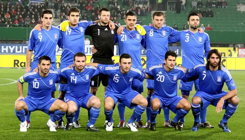 Drużyna piłkarska Grecji w niebieskich strojach pozuje do zdjęcia na boisku.