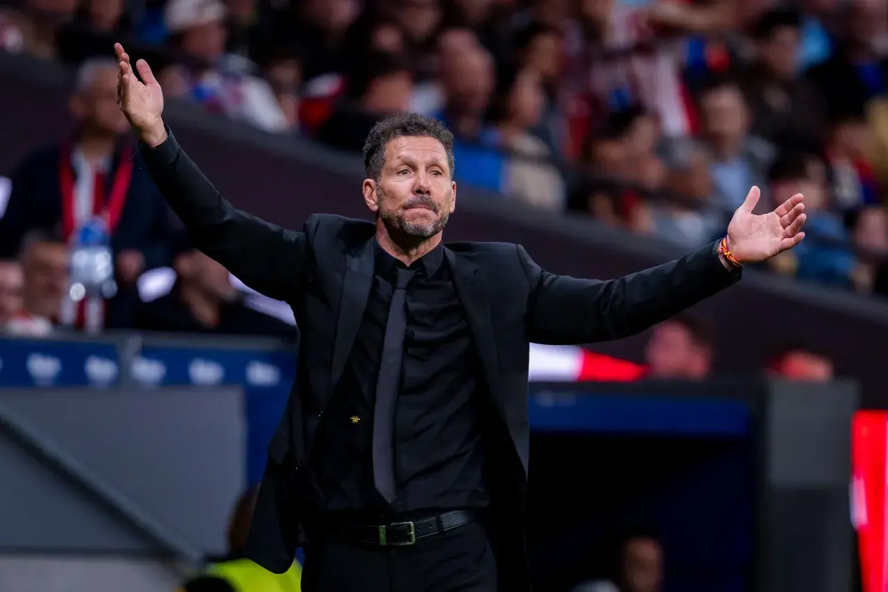 Diego Simeone, trener Atletico, w czarnym garniturze z rozłożonymi rękami, gestykuluje na boisku.