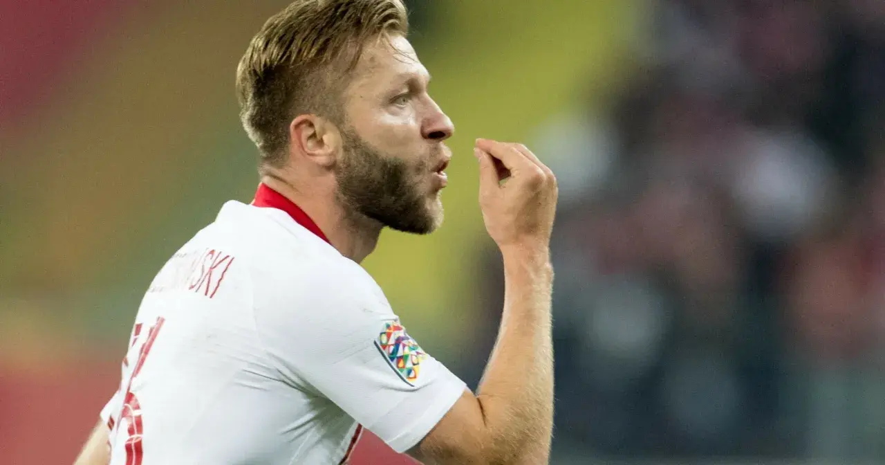 Piłkarz w białej koszulce z numerem 7, Jakub Błaszczykowski, pokazuje gest. Jego błyszczący wzrost na boisku to inspiracja dla wielu.